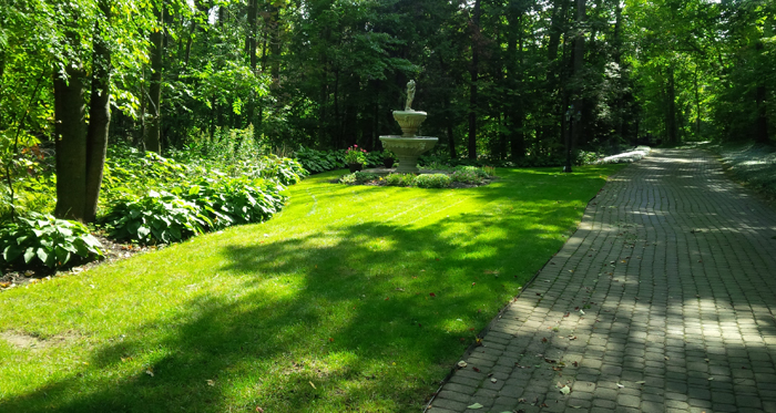 nicely cut lawn with cobblestone path way and multi-level water fountain in the background